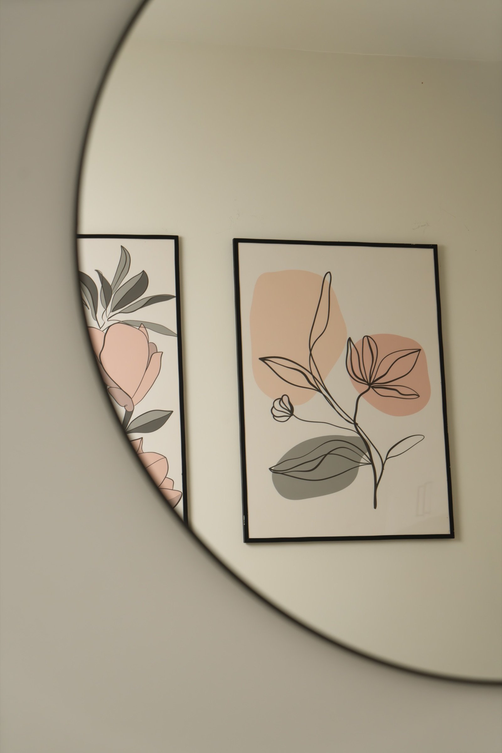 Round mirror reflecting a botanical line drawing on a pale studio wall